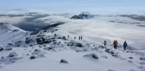 Climbers resting at a high-altitude camp with Mount Kilimanjaro's glaciated peak visible in the background
